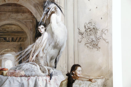 Surrealist fine art print titled “La Casa del Té” featuring a dreamlike interior filled with exotic birds, a monkey, and ethereal human figures gathered around an elaborate dining table. Soft neutral tones, dramatic animal symbolism, and ornate architectural details create a haunting contemporary surrealist atmosphere.